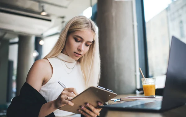 Mujer Rubia Enfocada Usando Pluma Para Escribir Portapapeles Mientras Está — Foto de Stock