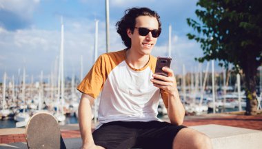 Modern cep telefonu cihazlı mutlu beyaz adam dışarıda dinlenmek için iyi bir gün geçiriyor. Moda güneş gözlüklü genç adam mobil teknoloji kullanıyor ve kablosuz bağlantısı var.