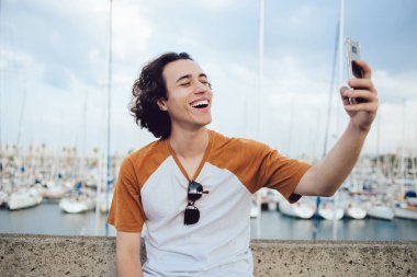 Öndeki kameraya gülümseyen başarılı blogcu, ağları paylaşmak için komik medya içeriği yaratırken mutlu hipster adam kendini Berth arka planında çekerken selfie görüntülerine tıklıyor.