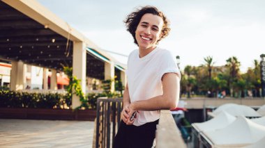 Barcelona 'da balkonun ahşap çitlerine yaslanırken kameraya bakıp gülümseyen rahat siyah saçlı adamın yan görüntüsü.