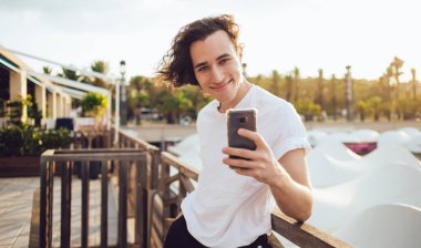 Barcelona 'daki modern terasta gülümseyen ve kameraya bakarken cep telefonuyla selfie çeken günlük kıyafetli genç adam.