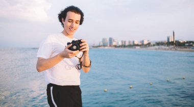 Kafkasyalı turist çevre fotoğraflama ve uygulama becerileri için modern kamerada ayarlama ayarları, deniz kenarında boş zamanlarında fotoğraf düzenleyen genç amatör