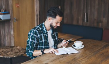 Olumlu, genç, sakallı, serbest çalışan, akıllı telefonları karıştıran, notları kontrol eden, kafenin modern çalışma alanında bir fincan kahveyle çalışan...