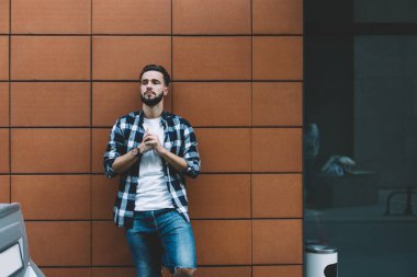 Düşünceli, şık, genç bir adam kollarını kavuşturup uzaklara bakıyor. Duvara ayak basıyor ve dışarıya dokunuyor.