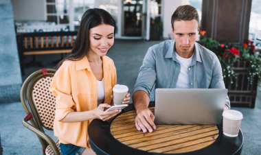 Laptop ve içerikli iş kadını kullanan, akıllı telefonuyla mesajlaşan ve açık havada birlikte oturan konsantre olmuş bir iş adamı.