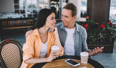 Akıllı telefon ve dizüstü bilgisayarlı rahat bir çift kahve içip hikayeler anlatıyor. İlgili kız arkadaşının birbirine baktığı omuz omuza.