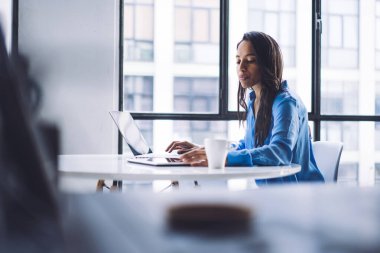 Çağdaş ofiste beyaz masada kahve içerken dizüstü bilgisayar ve tablet kullanan ciddi Afrikalı Amerikalı kadınların seçici odak noktası