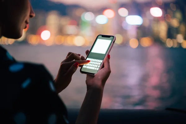 顔のない現代の女性は 夕暮れ時に遠く離れた照明付きの街並みでキーでテキストメッセージのためのスマートフォンを使用してカジュアルウェア — ストック写真