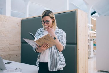 Barselona 'da üniversite kütüphanesinde okurken günlük kıyafetler ve gözlüklerle esniyor ve kitap okuyor.
