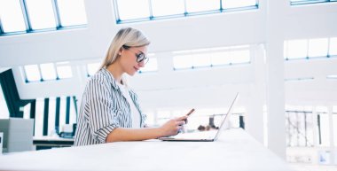 Barcelona 'daki modern kütüphanede araştırma projesi üzerinde çalışırken bilgisayarlı ve akıllı telefonlu zeki genç kadınların yan görüntüsü.