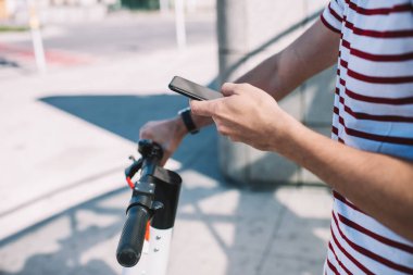 Sokakta dikilirken cep telefonundan mesaj gönderirken kol saati takan sıradan giyinmiş bir adam mobilet gidonu tutuyor.