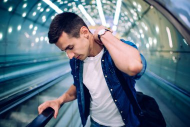 Üst kattaki şık elbiseli genç adam metro yürüyen merdivenlerinde duruyor. Işıklar ve spor çantasıyla.