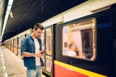 Kol saati olan sıradan giyinmiş bir adam metro istasyonunda ışıklarla beklerken cep telefonundan mesaj yolluyor.