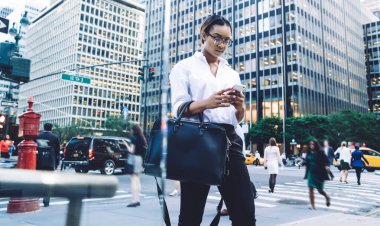 Yoğunlaşmış, genç, zeki, kısa saçlı, kısa saçlı, resmi kıyafetler giyen ve elinde cep telefonu olan bir kadın.