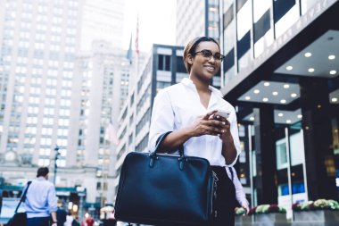 Resmi giysiler içindeki neşeli genç kadın, iş gününün ertesi günü iş yerinde güneş ışığında arkadaşından komik bir mesaj alıyor.