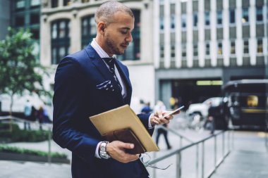 Düşük açılı özgüvenli, iyi giyimli, kağıt ve gözlüklü işadamı, şehir merkezindeki çağdaş ofis binasının bulanık girişine karşı caddede dikilirken ilgi ve akıllı telefonla iletişim kuruyor.