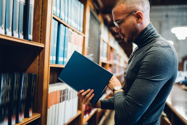 古い公共図書館の棚の近くに立って読書のための本を選択白人男性学生 知識を増加させるための文学を選択するアーカイブに学術教授の支出時間の側面ビュー — ストック写真