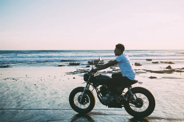 夏はビーチでバイクに乗りながら海辺の風景を楽しむカジュアルな服装で気楽な男性のオートバイの側面図 — ストック写真