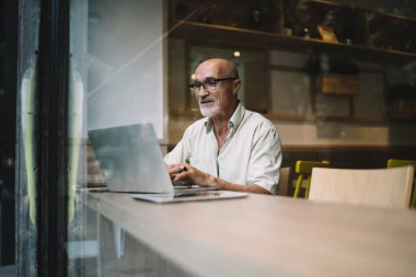 Konsantre olmuş, gözlüklü, bilgisayar klavyesinde yazı yazan gözü pek bir iş adamı. Masada aletlerle oturup ekrana bakıyor.