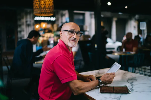 穿着休闲装 戴眼镜的大胡子男子在现代咖啡店看着平板电脑 望着别处的侧视图 — 图库照片