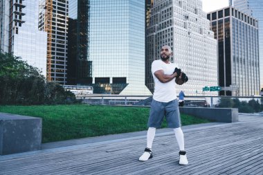 Spor kıyafetli atletik siyah erkek, sabah caddedeki ahşap patikaya dik dik bakarak silah tatbikatı yapıyor.