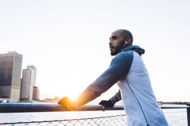 Kulaklık takmış, spor giysiler giymiş, set seti üzerinde antrenmandan sonra dinlenen ve yansıtıcı bir şekilde başka yöne bakan düşünceli, uysal bir erkek.