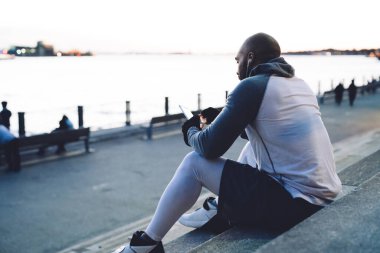 Spor düşkünü Afrikalı Amerikalı özel eğitimli bir adamın cep telefonu taşın üzerinde otururken yan görüntüsü