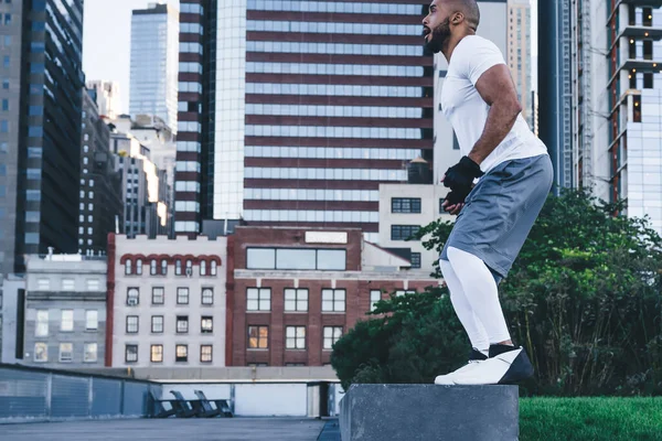 城市背景下穿着运动服做跳跃运动的非洲裔美国成年男子体形的侧观 — 图库照片