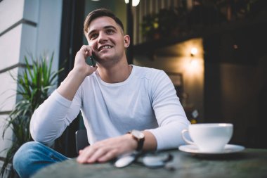 Şehir kafeteryasının terasında bir fincan çayla dinlenirken gündelik kıyafetlerle telefona cevap veren iyimser genç adam.