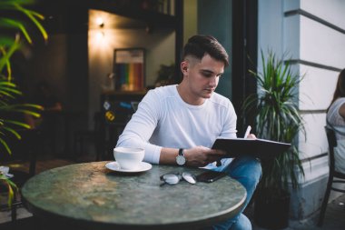 Gündelik giysiler içinde, kahve içen ve modern kafe 'nin yazlık planlama bölümünde günlük programı dolduran serbest çalışan bir erkek.
