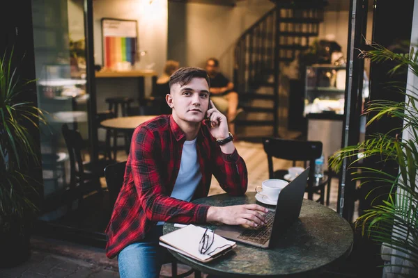 Задумчивый Мужчина Повседневной Одежде Сидит Столом Кафе Пользуясь Ноутбуком Разговаривая — стоковое фото