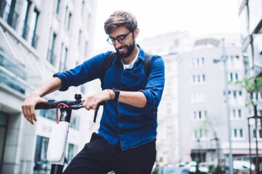 Düşük açılı, sakallı, gözlüklü ve sırtında elektrikli scooter olan genç bir erkek.