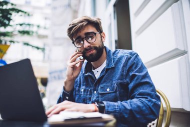 Yetişkinlerin uzaktan kumandalı çalışanları sokakta otururken ve taşınabilir bilgisayarda yazarken ve kameraya bakarken cep telefonuyla konuştur.