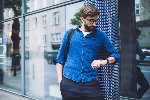 Young Bearded Male Eyeglasses Backpack Shoulder Looking Smartwatch While Waiting — Stock Photo, Image