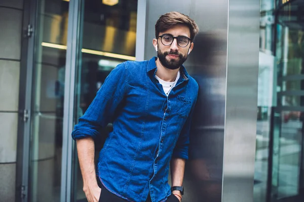 Amistoso Joven Barbudo Gafas Auriculares Mirando Cámara Mientras Apoya Columna —  Fotos de Stock