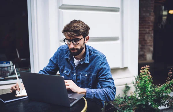 Joven Hombre Traje Casual Gafas Usando Portátil Tomando Notas Mientras —  Fotos de Stock