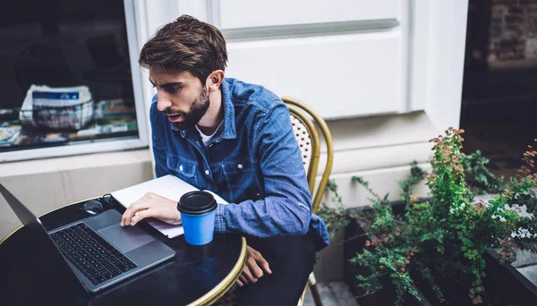 穿着休闲装的年轻人专心致志地盯着笔记本电脑屏幕 沉浸在工作过程中 喝一杯咖啡就可以上桌了 — 图库照片