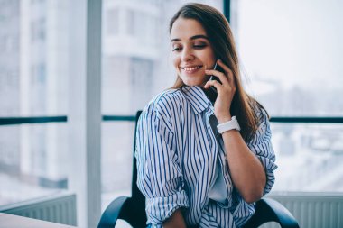 Modern ofisteki dostça akıllı telefon konuşmaları sırasında çalışma alanı deneyimini tartışan güzel bir bayan stajyer hücresel iletişim kurduğu için 4G 'ye bağlanan modaya uygun tişörtlü akıllı bir kadın.