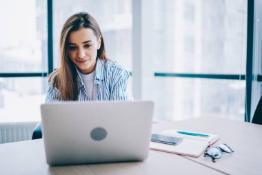 Akıllı gündelik kıyafet giyen yetenekli bayan öğrenci, üniversitenin ders çalışması için bilgi verici web araştırması yapmak için dizüstü başvuru kullanıyor, kablosuz internet sayfasını karıştıran beyaz kadın