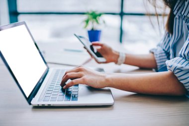Bulanık cep telefonu ve boş ekranlı maket dizüstü bilgisayarla sosyal ağ üzerinden kadın arama web bilgilerinin kırpılmış görüntüsü, rezervasyon ve bankacılık yapmak için kablosuz ağa bağlanan kadın