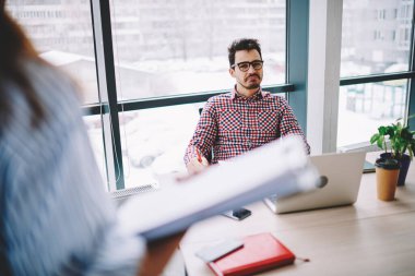 Optik gözlüklü etkileyici işverenin göz düzeltme bilgileri ofis içi iş görüşmesi sırasında iletişim kuran kırpık stajyerden, masadaki dizüstü bilgisayardan geliyor.