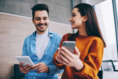 Modern akıllı telefon ve dokunmatik ped ile içerik metnini okumak için kapalı mekanlarda wifi internete bağlanan mutlu hipsterlar, ağ kurarken online rezervasyonları tartışan gülümseyen adam ve kadın