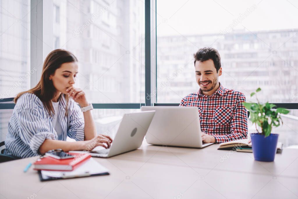 Caucasian male and female colleagues in smart casual wear sitting at table desktop and collaborating on web project, skilled IT professionals connecting to office internet for creating program code