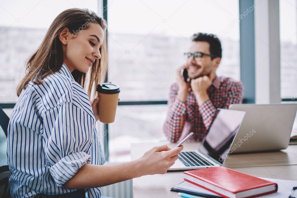 Smart casual female employee with coffee to go in hand connecting to to office internet for installing application notification during social networking, millennial woman messaging via cellphone