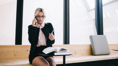 Optik gözlüklü beyaz girişimci not defterinden bilgi topluyor, gururlu bayan sahibi akıllı telefon uygulaması ve 4G bağlantısı kullanarak partneriyle mobil konuşma yapıyor.