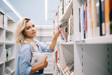 Kitapçıdan kitap almak için kitap seçen güzel kız öğrencilerin yarım boy portresi, Kafkasyalı kütüphaneci kitaplıktan en çok satan edebiyat kitapçılarını seçerek sipariş topluyor.