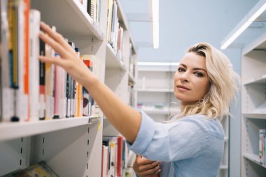 Kitapçıdan kitap almak için kitap seçen güzel kız öğrencilerin yarım boy portresi, Kafkasyalı kütüphaneci kitaplıktan en çok satan edebiyat kitapçılarını seçerek sipariş topluyor.