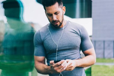 Kaslı vücut geliştirici açık hava egzersizi sırasında spor bildirimleri okuyor çevrimiçi müzik dinlemek için 4g internet kullanıyor, Kafkas erkeksi bir adam hayatta pratik yapmak için video eğitimi izliyor.