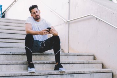 Aktif görevde olan erkek sporcu, açık hava antrenmanından sonra ara veren cep telefonundan bildirimleri kontrol ederken, kulaklıklı sporcu akıllı telefon çalarına medya müziği indirirken posta mesajı gönderiyor.