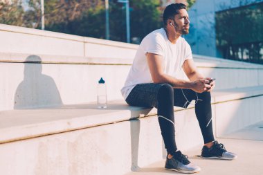 Elektronik stereo ekipmanları dinleyen düşünceli erkek vücut geliştirici idman üzerinde kafa yoran kişisel antrenörden sesli mesaj aldı.